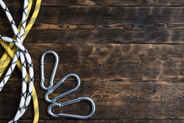 Carabiners and safety rope on a brown wooden board background with copy space. - Фото, изображение