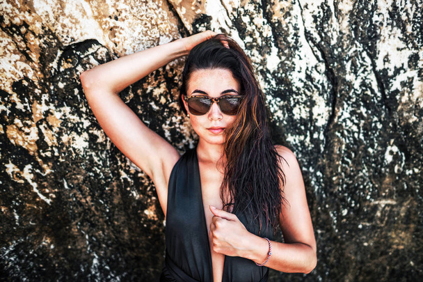 Pretty brunette pan asian girl in black swimsuit relaxing under the rock on the beach - Foto, Imagem