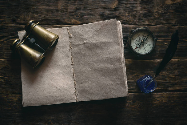 Blank traveler notebook, binoculars and nautical compass on a wooden table background mockup. Adventurer notes.  - Foto, Bild