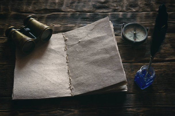 Blank traveler notebook, binoculars and nautical compass on a wooden table background mockup. Adventurer notes.  - 写真・画像