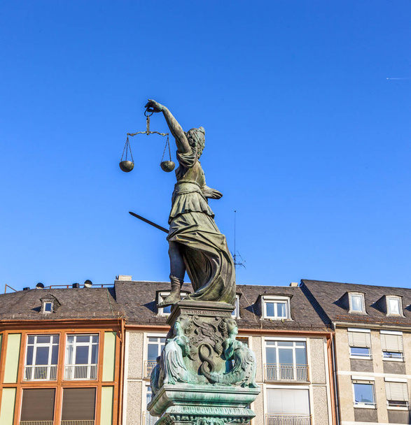 Lady Justice de pie en la fuente bajo el cielo azul de Frankfurt como símbolo de justicia
 - Foto, Imagen