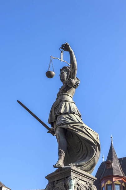 Lady Justice de pé na fonte sob o céu azul em Frankfurt como um símbolo de justiça
 - Foto, Imagem