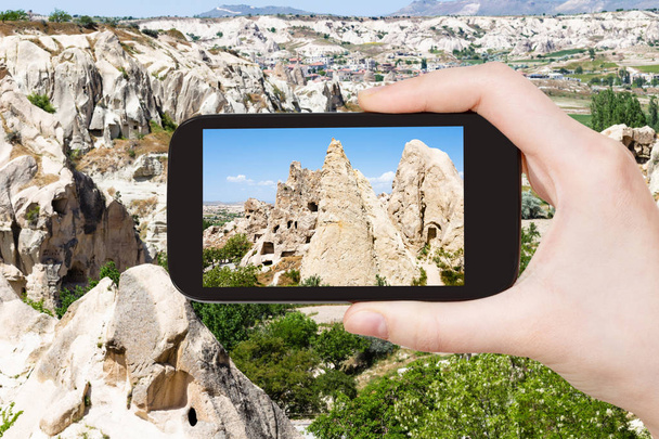 travel concept - tourist photographs of ancient rock-cut monastic settlement near Goreme town in Cappadocia on smartphone in Turkey in spring - Foto, immagini