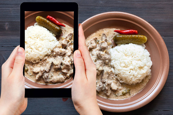 utazási koncepció - látogatói fényképek orosz konyha étel marha Stroganoff (marha Stroganov, Befstroganov) darab párolt hús tejföl főtt rizs okostelefonra - Fotó, kép