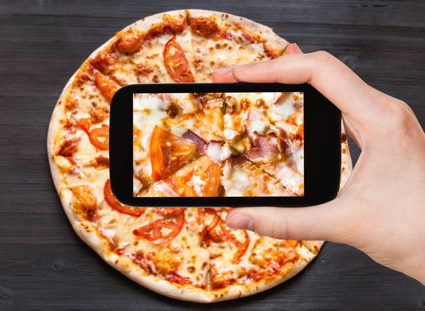 matkakonsepti - kävijäkuvia Pizzan täyttämisestä pekonilla ja tomaateilla lähikuva älypuhelimella
 - Valokuva, kuva