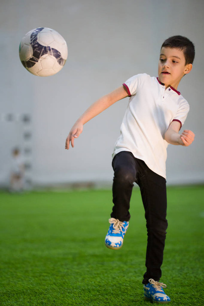 Ένα μικρό αγόρι που ρίχνουν την μπάλα στο πεδίο του παίζοντας ποδόσφαιρο με τα άλλα παιδιά - Φωτογραφία, εικόνα