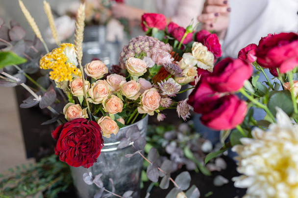 金属製のバケツの花をクローズ アップ。花屋の職場。バラ、キク、カーネーション、他の花で花束をアレンジする女性。マスター クラスやコースのフローリストの先生 - 写真・画像