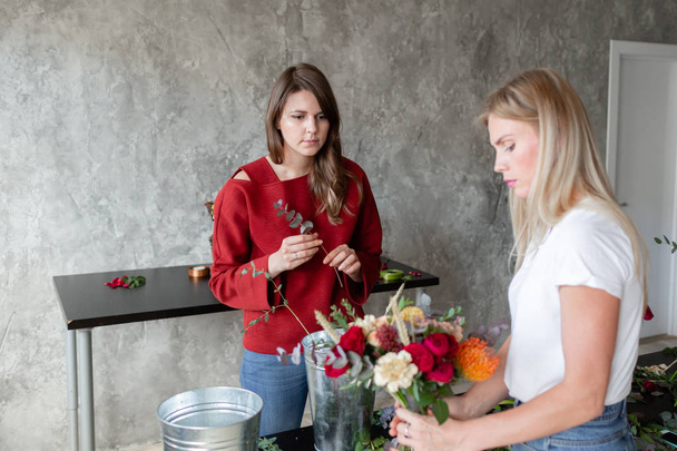 Floristik-Arbeitsplatz. Frau arrangiert einen Strauß mit Rosen, Chrysanthemen, Nelken und anderen Blumen. Lehrer und Floristikstudent in Meisterkursen oder Kursen - Foto, Bild