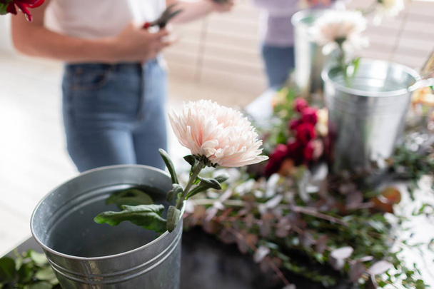 Γκρο πλαν λουλούδια σε έναν μεταλλικό κουβά. Ανθοπωλείο στο χώρο εργασίας. Γυναίκα τακτοποίηση ένα μπουκέτο με τριαντάφυλλα, χρυσάνθεμα, Γαρύφαλλο και άλλα λουλούδια. Δάσκαλος του Ανθοπωλεία master μαθήματα ή μαθήματα - Φωτογραφία, εικόνα