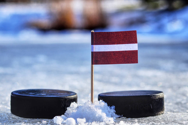 A Latvia flag on toothpick between two hockey pucks.  A Latvia will playing on World cup in group B. 2019 IIHF World Championship in Slovakia. - Photo, Image