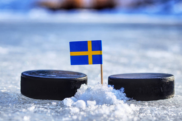 A Sweden flag on toothpick between two hockey pucks.  A Sweden will playing on World cup in group B. 2019 IIHF World Championship in Slovakia - Photo, Image
