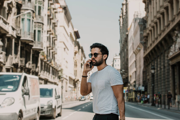 Young urban professional man using smart phone. Hipster coworker holding mobile smartphone using app texting sms message wearing sunglasses - Foto, Imagem