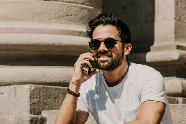 Handsome bearded hispanic man using mobile smartphone for surfing web internet, making call and looking digital city map. Male using electronic device in travel - Fotoğraf, Görsel