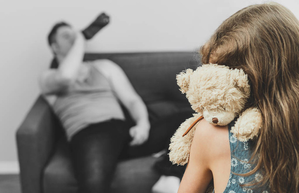 Little girl with toy standing in front of her drunk father. - Foto, Bild