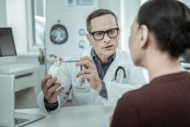 Confused doctor holding gypsum model of the main organ of the person - Foto, Bild