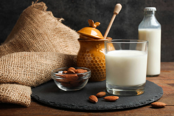 Vaso de leche, tarro de miel y almendras sobre pizarra sobre mesa de madera sobre fondo negro
. - Foto, imagen