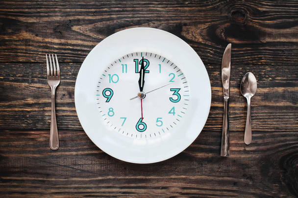 Twelve hour intermittent fasting time concept with clock on plate over a rustic wooden table / background. Top view.  - Foto, afbeelding
