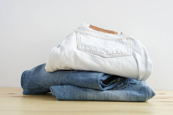 Stapel jeans in verschillende kleuren op houten tafel textuur en witte achtergrond isolatie - Foto, afbeelding