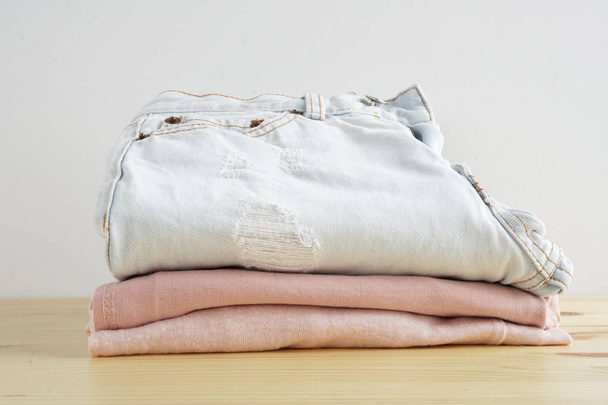 Stack van kleding. Jeans, hemd, jurk, trui over houten tafel en witte achtergrond isolatie - Foto, afbeelding