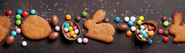 Easter greeting card backdrop with colorful gingerbread cookies, chocolate eggs and candies. Top view on stone table - Photo, Image