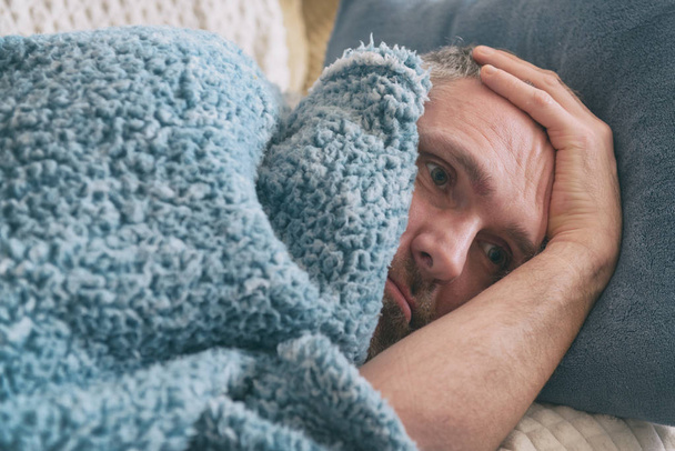 Ώριμο άνδρα που πάσχουν από κατάθλιψη βρίσκεται δυστυχώς καλύπτεται με μια κουβέρτα στο κρεβάτι του  - Φωτογραφία, εικόνα