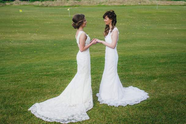 Two beautiful brides holding hands on the green field of the golf club - Photo, Image