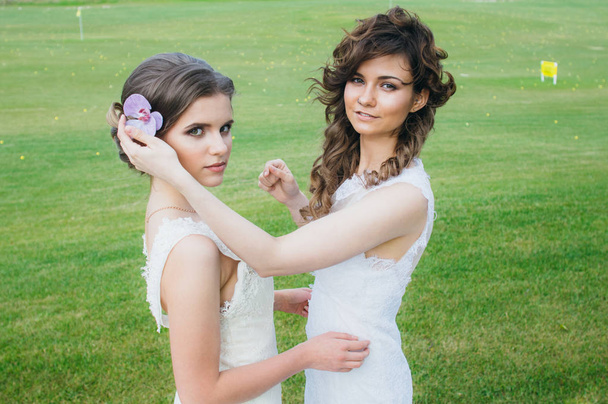 Две красивые невесты корректируют волосы на зеленом поле гольф-клуба
 - Фото, изображение