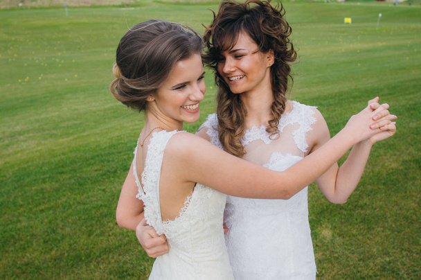 Dvě krásné nevěsty tančí na zelené louce v golfovém klubu - Fotografie, Obrázek