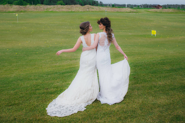 Two beautiful brides embracing on the green field of the golf club - Photo, Image