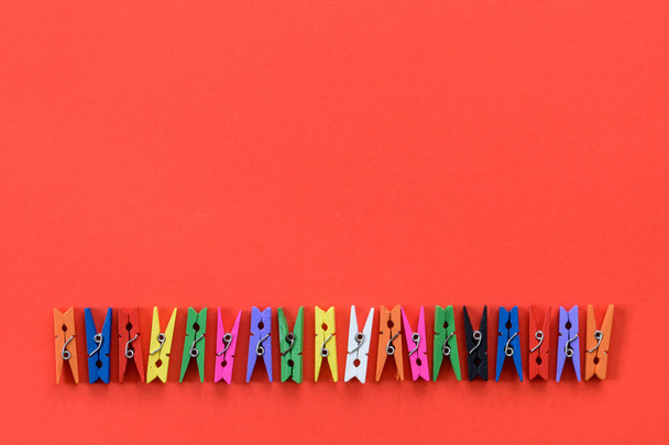 A row of colorful wooden clothespins on a red background and copy space. - Foto, imagen