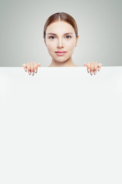 Pretty woman showing white empty paper banner background and looking at camera, studio portrait - Foto, afbeelding