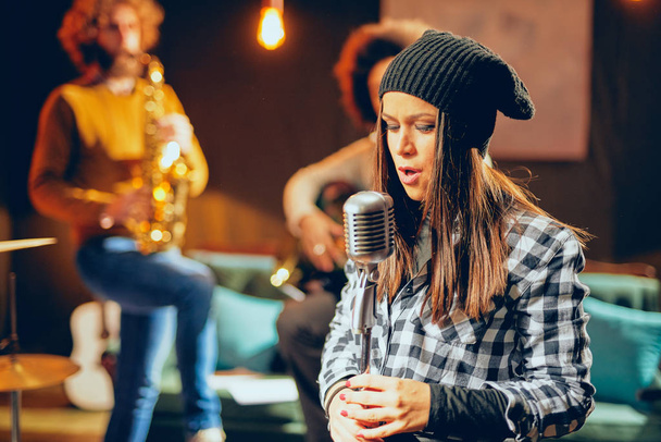 Práctica de la banda en casa estudio. Mujer cantando mientras el resto de la banda toca instrumentos
. - Foto, Imagen