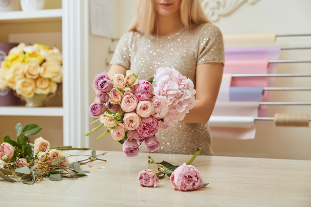 gedeeltelijke weergave van bloemist maken bouquet van rozen en pioenrozen op werkplek - Foto, afbeelding
