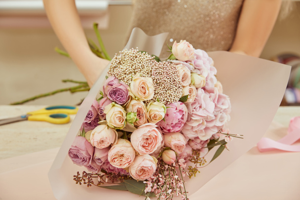  florist wrapping bouquet of roses and peonies at workspace - Photo, image