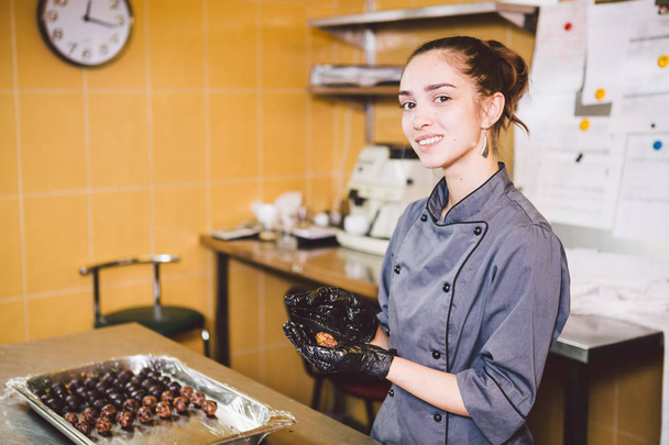 Subject profession and cooking pastry. young Caucasian woman with tattoo of pastry chef in kitchen of restaurant preparing round chocolate candies handmade truffle in black gloves and uniform. - 写真・画像