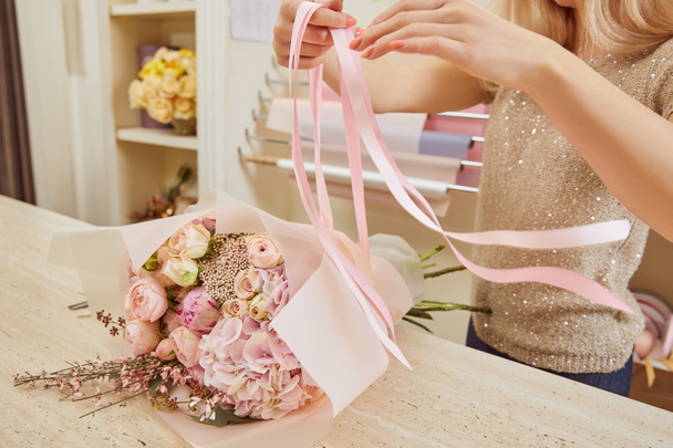 partial view of florist tying ribbons on bouquet of roses and peonies  - Фото, зображення