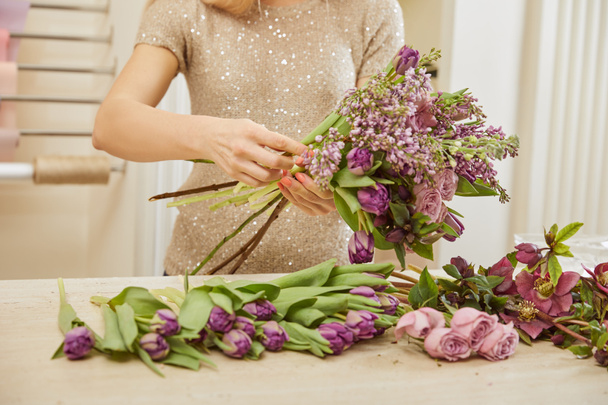 partial view of florist making bouquet of tulips, peonies and lilac at flower shop - Фото, изображение