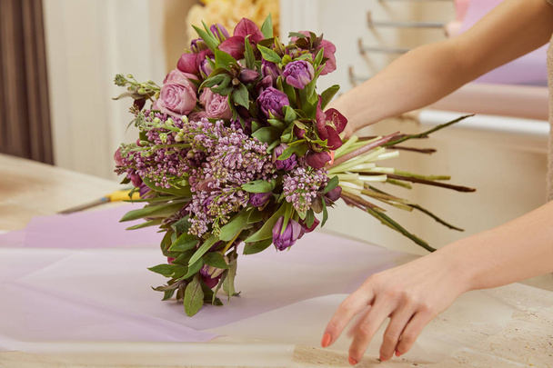 cropped view of florist wrapping  bouquet of tulips, peonies and lilac - Photo, Image