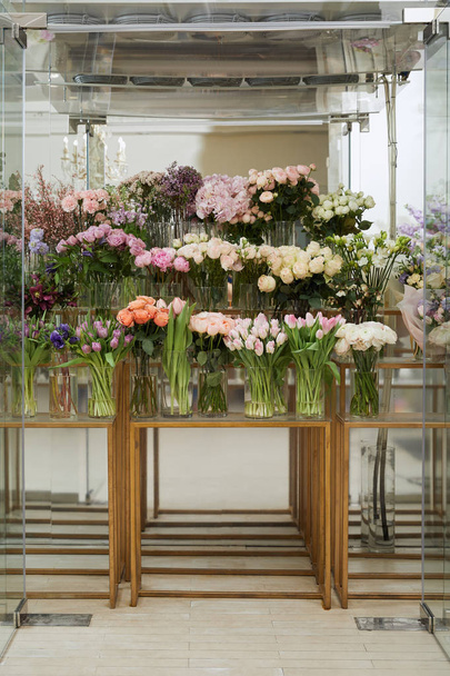 τριαντάφυλλα, τουλίπες και παιώνιες σε βάζα σε γυάλινα τραπέζια - Φωτογραφία, εικόνα