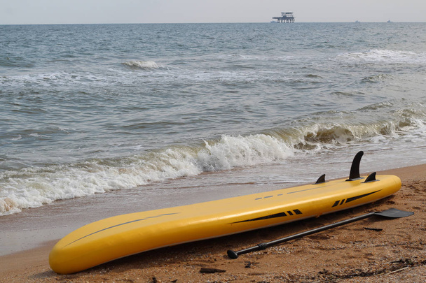 Żółty supboard znajduje się na piaszczystej plaży obok wiosło. - Zdjęcie, obraz