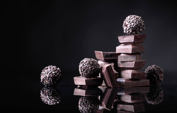 Bonbons au chocolat avec des morceaux de chocolat cassés sur fond réfléchissant noir. Espace de copie
. - Photo, image