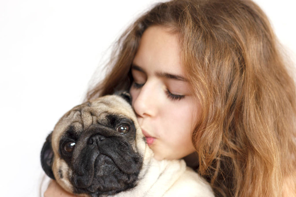 Linda chica adolescente abrazando y besando perro pug sobre fondo blanco
 - Foto, Imagen