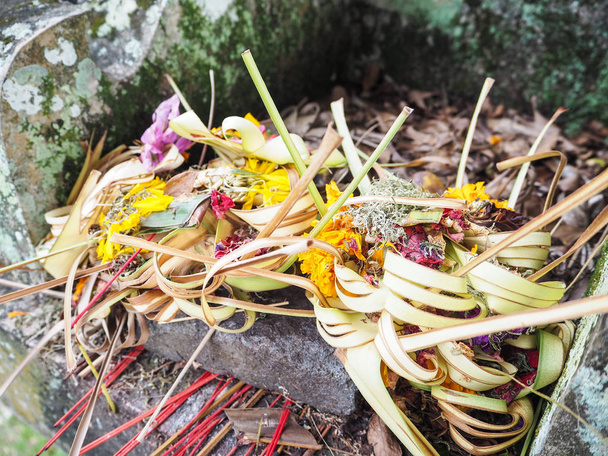 Pile di vecchie offerte canang sari essiccate alla base di una statua in pietra, Amed, Bali, Indonesia
 - Foto, immagini
