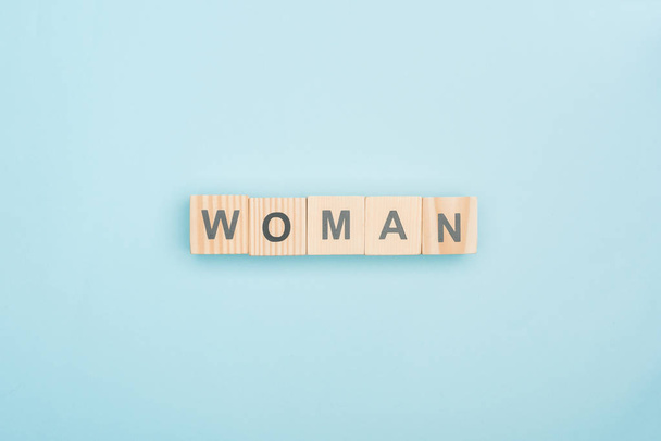 top view of woman lettering made of wooden cubes on blue background - Fotó, kép