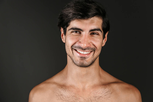 Image of a handsome naked young smiling man posing isolated over dark wall background. - Foto, immagini
