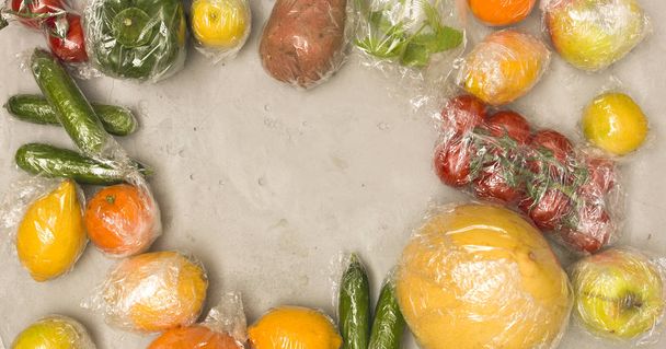 pile of fruits and vegetables wrapped in plastic foil on concrete background, plastic environmental pollution concept  - Foto, Imagem