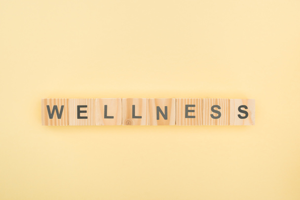 top view of wellness lettering made of wooden cubes on yellow background - Fotoğraf, Görsel