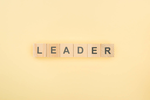 top view of leader lettering made of wooden cubes on yellow background - Foto, afbeelding