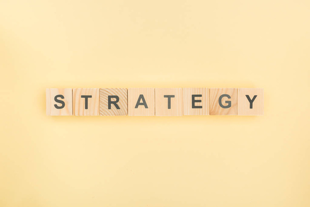 top view of strategy lettering made of wooden cubes on yellow background - 写真・画像