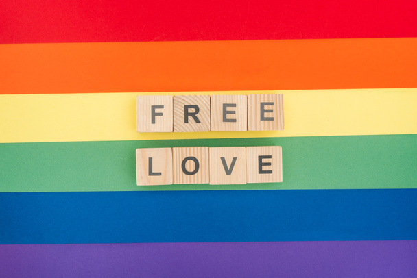 bovenaanzicht van de vrije liefde letters gemaakt van houten blokken op papier regenboog achtergrond - Foto, afbeelding